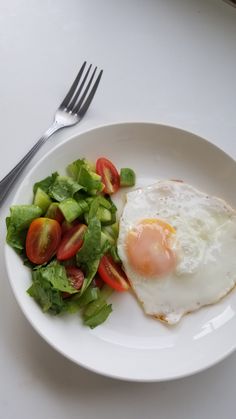 a white plate topped with an egg and salad next to a fork on top of a table