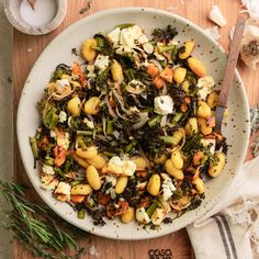 a white bowl filled with vegetables on top of a wooden table next to utensils