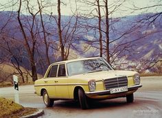 an old yellow car is parked on the side of the road in front of some trees