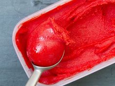 a scoop of red ice cream in a plastic container with a spoon on the side