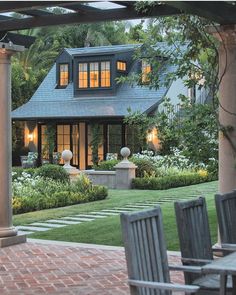 an outdoor patio with wooden chairs and brick walkway leading to the front door of a house