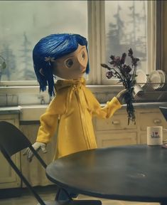 the doll is holding flowers in her hand at the kitchen table and looking out the window