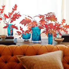 there are three vases with red leaves in them on the table next to books