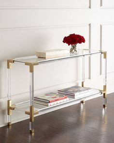 a glass table with some books and a red rose on it in front of a white wall