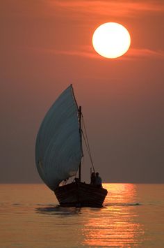 a small sailboat in the middle of the ocean at sunset or sunrise with people on it