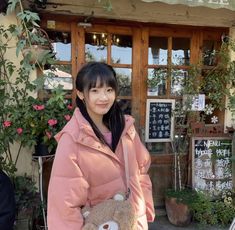 a woman standing in front of a store holding a teddy bear bag and smiling at the camera