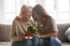 two women are sitting on a couch and one is holding a bouquet of tulips