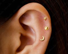 a woman's ear with two small stars and a crescent on the middle one