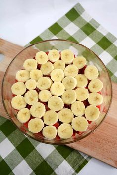 a glass bowl filled with sliced bananas on top of a wooden cutting board next to a green and white checkered tablecloth