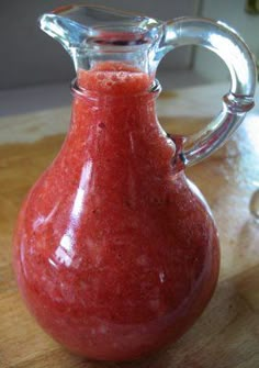 a glass pitcher filled with red liquid on top of a wooden table