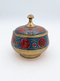 a blue and red vase with gold trimmings on it's lid, sitting on a white surface