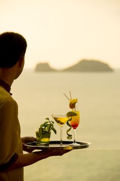 a man holding a tray with two drinks on it and another drink in the background