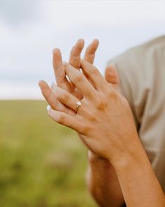 a woman is holding her hands together in the middle of an open field with grass