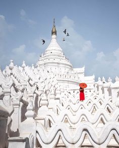 a person with an umbrella standing in front of a white building that has birds flying around it