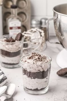 two desserts in small glass containers on a counter with spoons and utensils