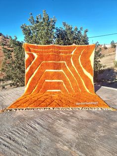 an orange and white blanket sitting on top of a wooden table next to some trees