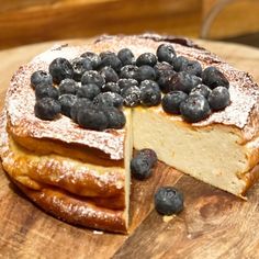 a cake with blueberries and powdered sugar on top sits on a cutting board