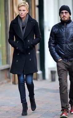 a man and woman are walking down the street in winter clothes, one is wearing a black coat