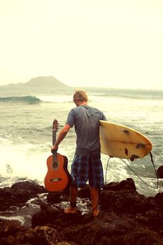 a man holding a surfboard standing on top of a rocky beach next to the ocean