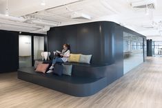 a woman sitting on a couch in an office reading a book and looking at her phone