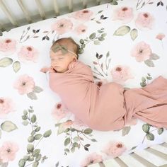 a baby sleeping in a crib with pink flowers on it