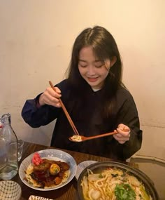 a woman sitting at a table eating food with chopsticks