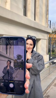 a woman taking a selfie with her cell phone in front of a building on the street