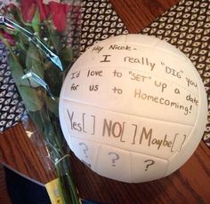 a bouquet of flowers sitting next to a volleyball on top of a wooden table with writing on it