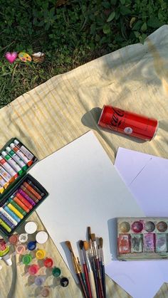 an artist's supplies including watercolors, paint and paper on a blanket