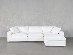 a white sectional sofa with pillows on the top and bottom, in front of a gray wall