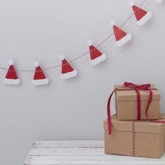 two boxes with christmas hats on them are sitting next to a string of paper santa's hats