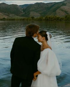 a bride and groom standing next to each other in front of a body of water