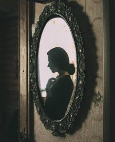 a woman standing in front of a mirror with her shadow on the wall behind it