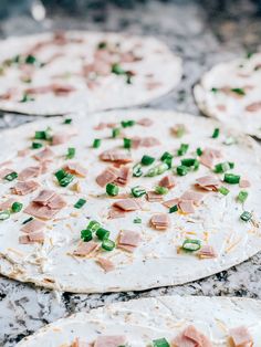 several pizzas with ham and green onions on them sitting on a counter top, ready to go into the oven