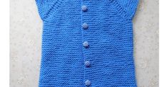 a blue knitted vest with buttons on the front and back, hanging up against a wall