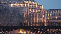 a bridge over a river in front of a large building at night with lights on