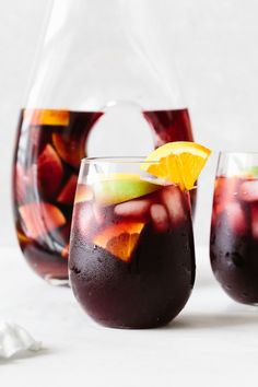 two glasses filled with liquid and fruit sitting on a white surface next to each other