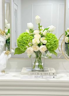 a vase filled with white and green flowers on top of a table next to a mirror