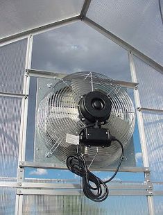 a fan sitting on top of a metal structure next to a skylight with clouds in the background