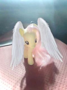 a little pony with white wings sitting on top of a pink tableclothed surface