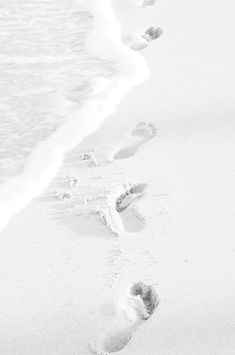 footprints in the sand near the water and an ocean shore with two people walking on it