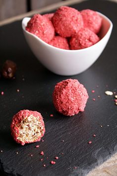 three balls of food sitting on top of a black board next to a bowl of nuts