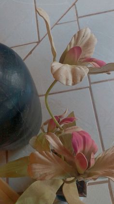 a vase filled with flowers sitting on top of a tiled floor next to a plant