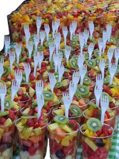 there are many plastic forks in cups with fruit on the table and checkered cloth