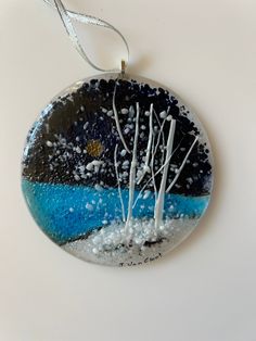 a glass ornament hanging on a white surface with water and trees in the background