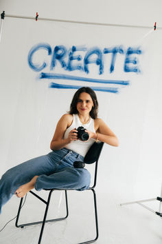 a woman sitting in a chair holding a camera and posing for a photo with the words create on it