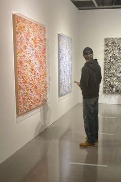 a man looking at art on display in an art gallery with two large paintings behind him