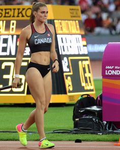 a woman walking across a track with a tennis racquet in her hand while wearing a black sports bra