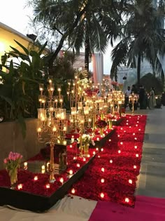 many candles are lit on the ground in front of red flowers and greenery at an event