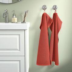 two orange towels hanging on the wall next to a white cabinet and sink in a bathroom